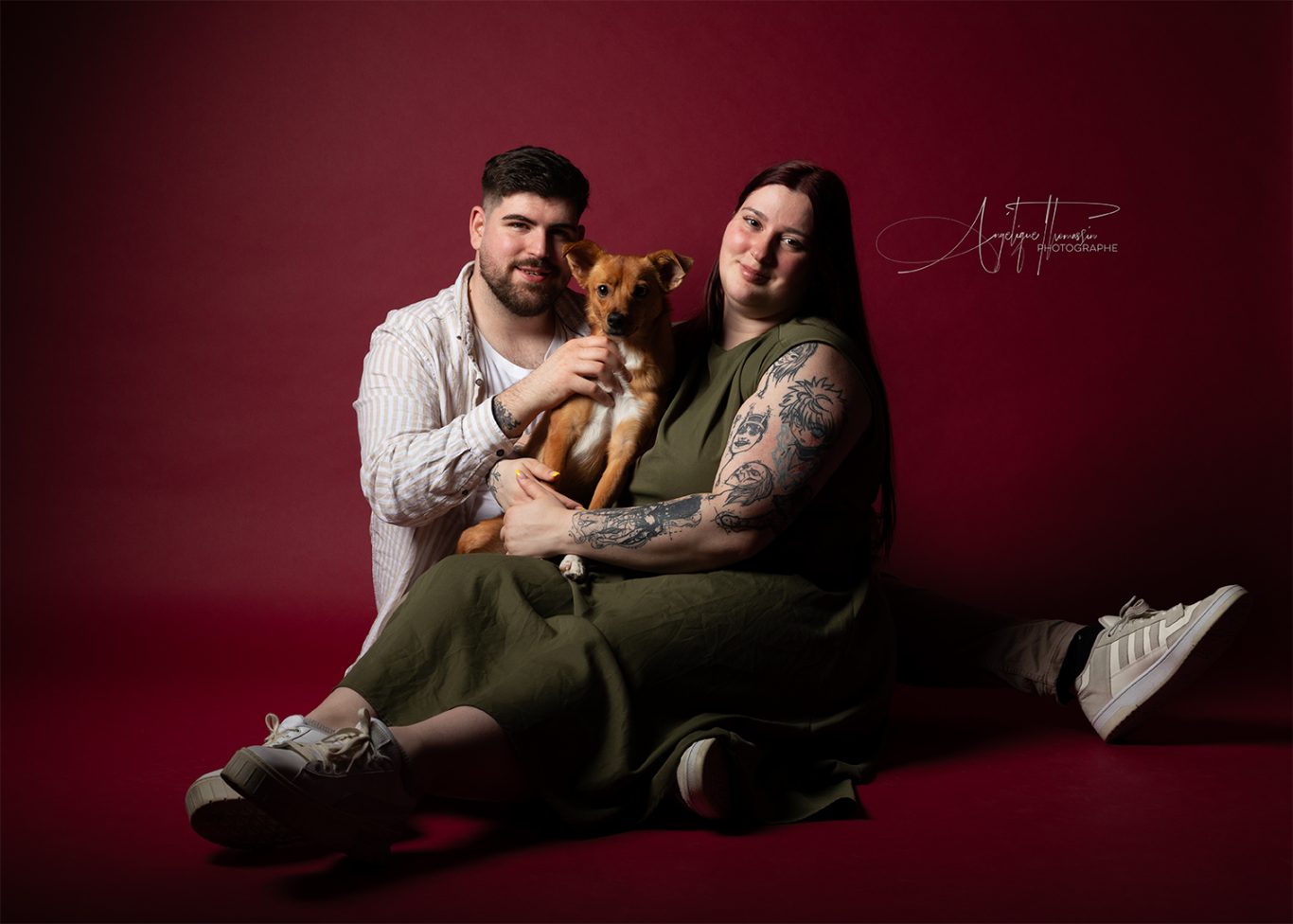 Juliette, Guillaume et Lilo Un couple souriant avec un chien sur fond rouge. L'homme porte une chemise, la femme une robe.