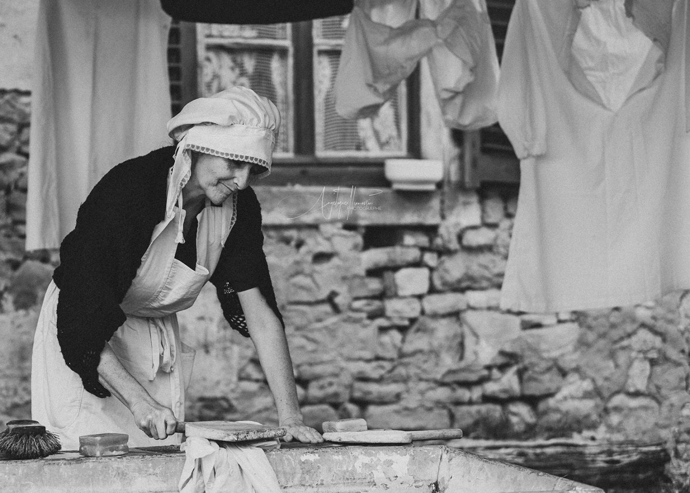 Xaronval village 1900 Femme en tablier préparant de la nourriture dans un environnement rustique.
